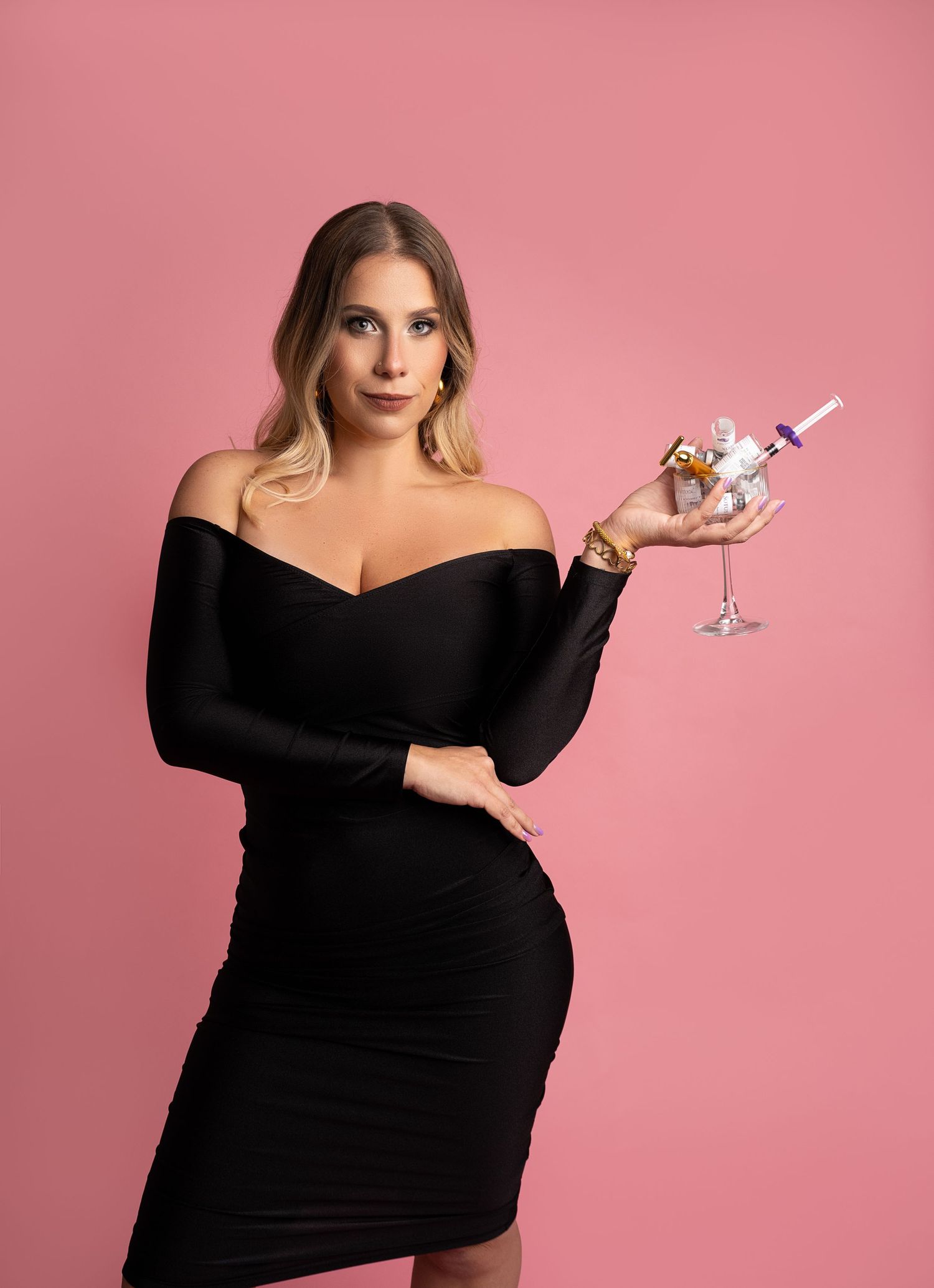 Woman in black dress poses with cocktail against pink backdrop.