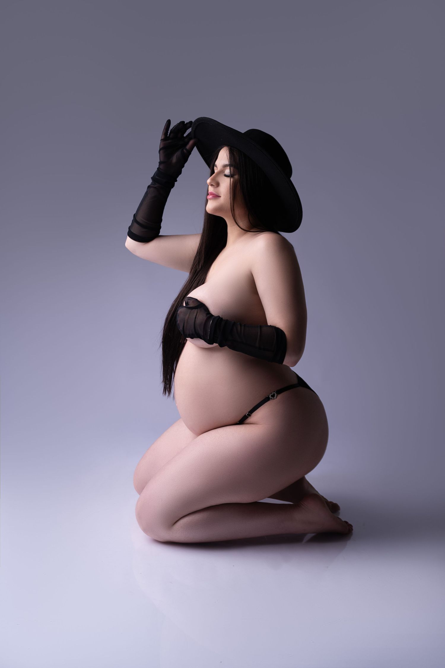 Dynamic maternity portrait with flowing black hair against light backdrop.