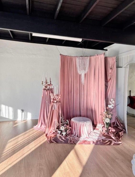 Elegant pink velvet drape backdrop with chandelier, floral arrangements, and sequin tablecloth for wedding decor.