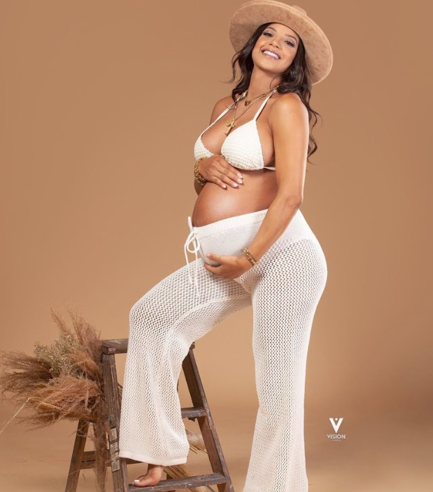 Maternity photo shoot featuring a white crochet dress against a warm brown backdrop with pampas grass decor.