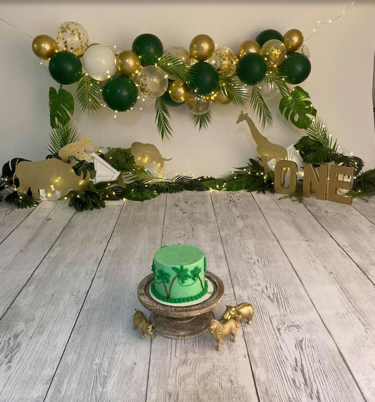 Green and gold balloon arch decorating a white wooden floor with festive party setup.