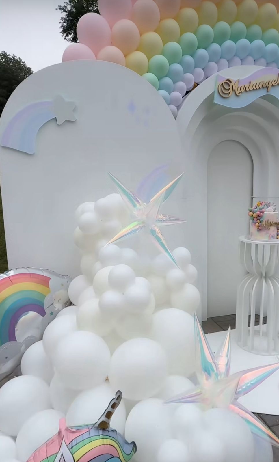 Pastel balloon arch installation with white cloud-like balloons and iridescent accents creates a dreamy rainbow party backdrop.
