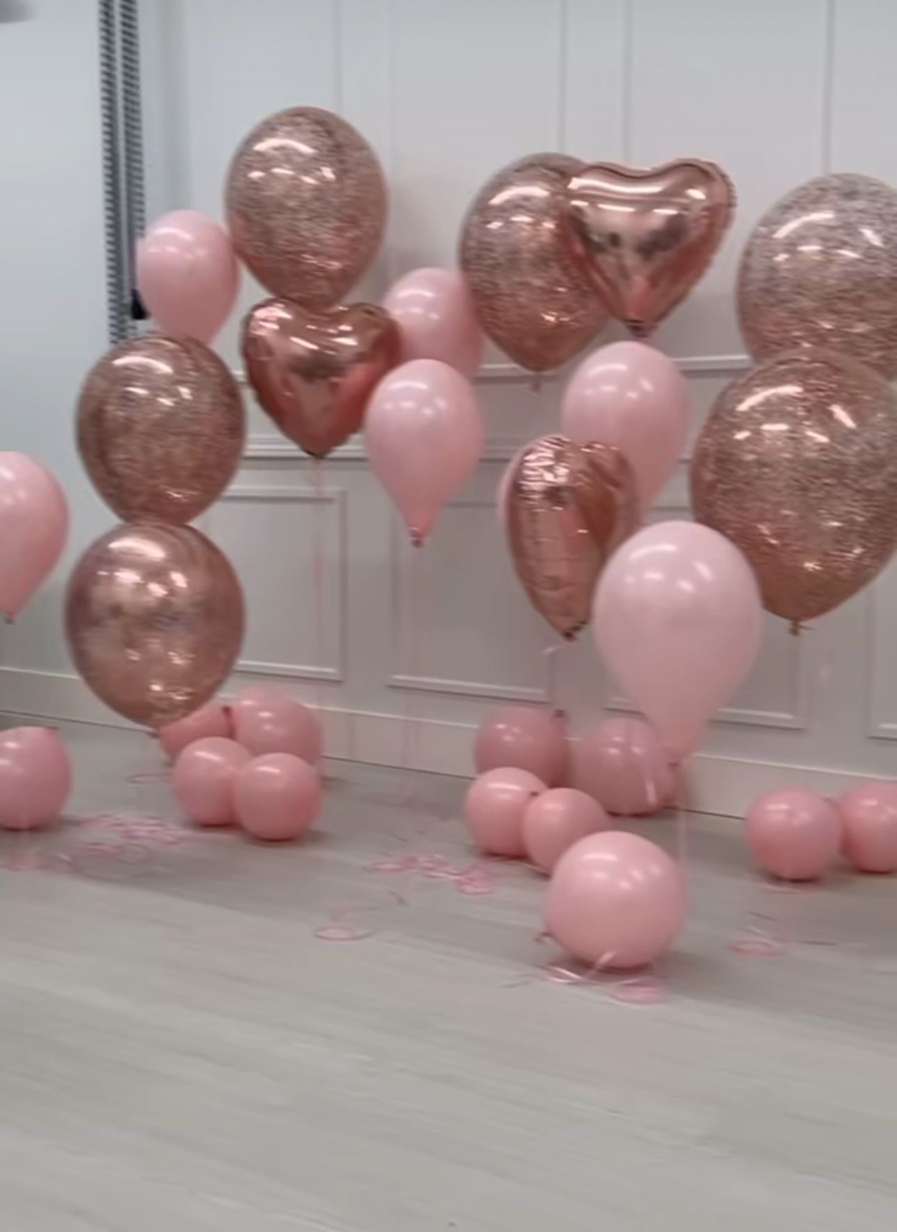 Pink and rose gold heart-shaped balloons arranged against a white wall for party decoration.
