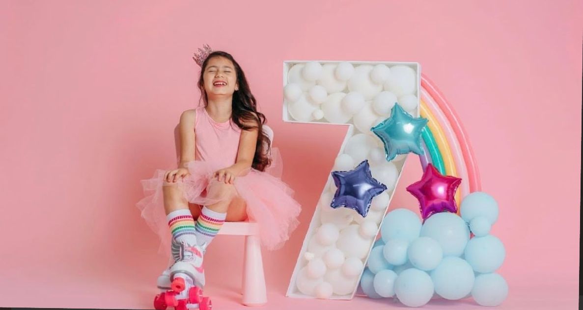 Festive pink backdrop with balloons, stars, and a rainbow creating a magical party setting.