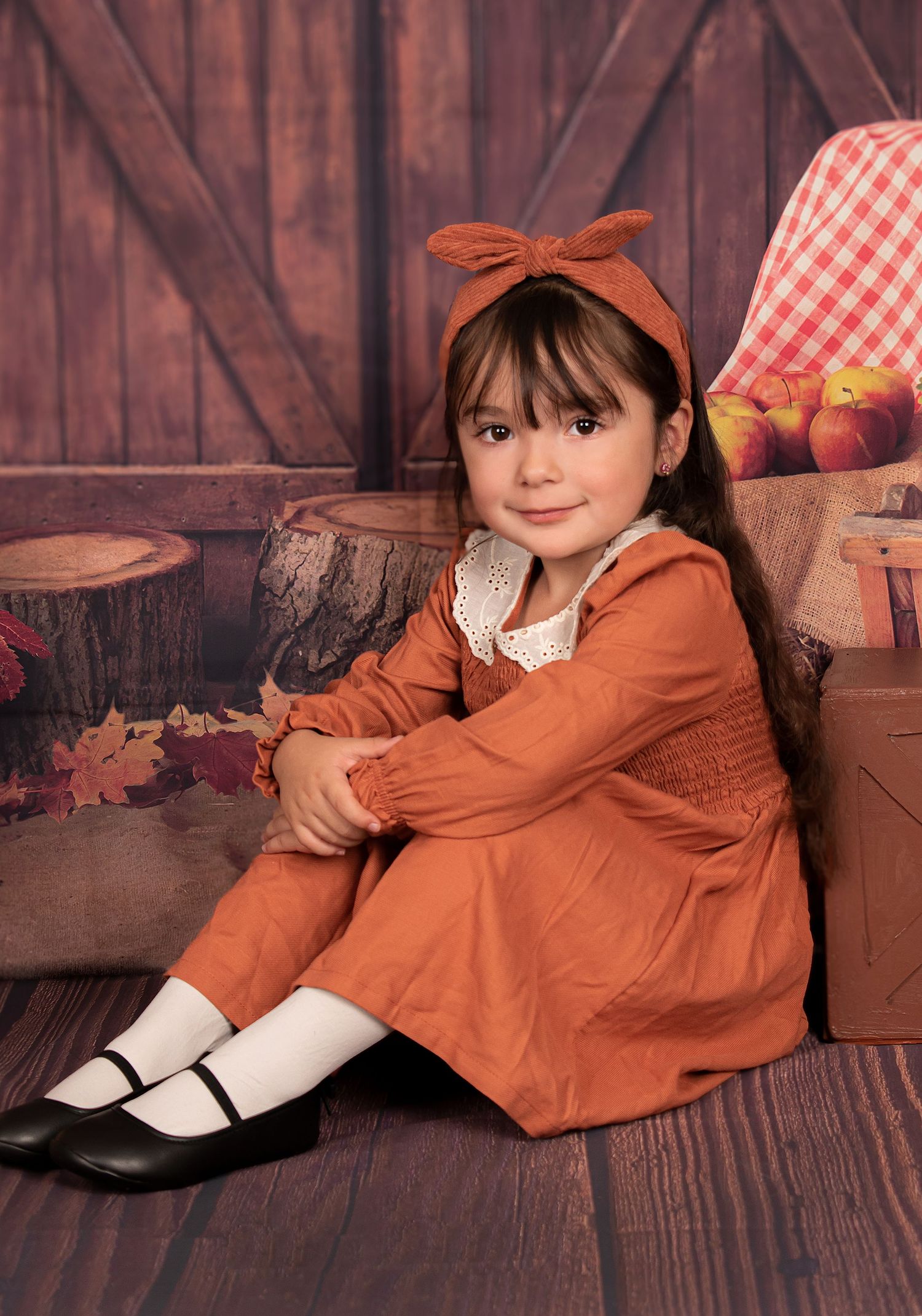 Autumn themed portrait with orange dress and bow against rustic wooden background.
