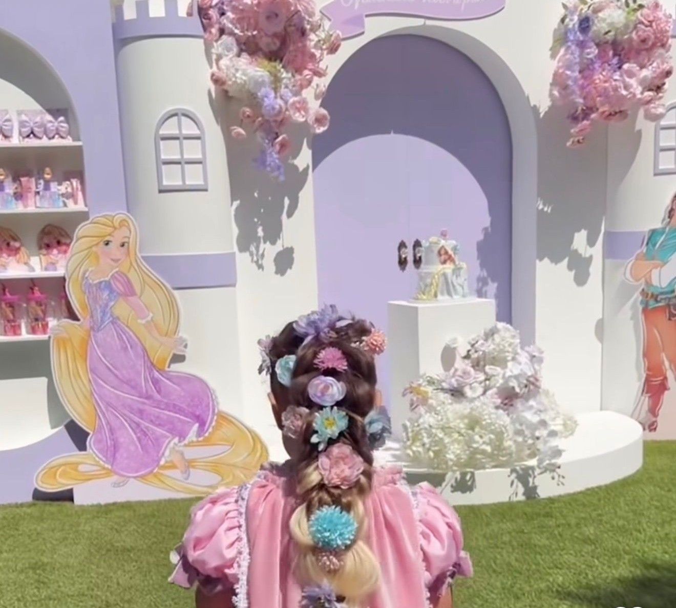 A child with floral hair accessories poses before a Rapunzel display at a princess-themed castle backdrop.