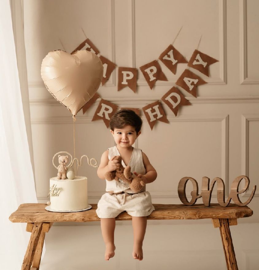 A rustic first birthday setup with wooden bench, cream heart balloon and Happy Birthday banner in brown tones.