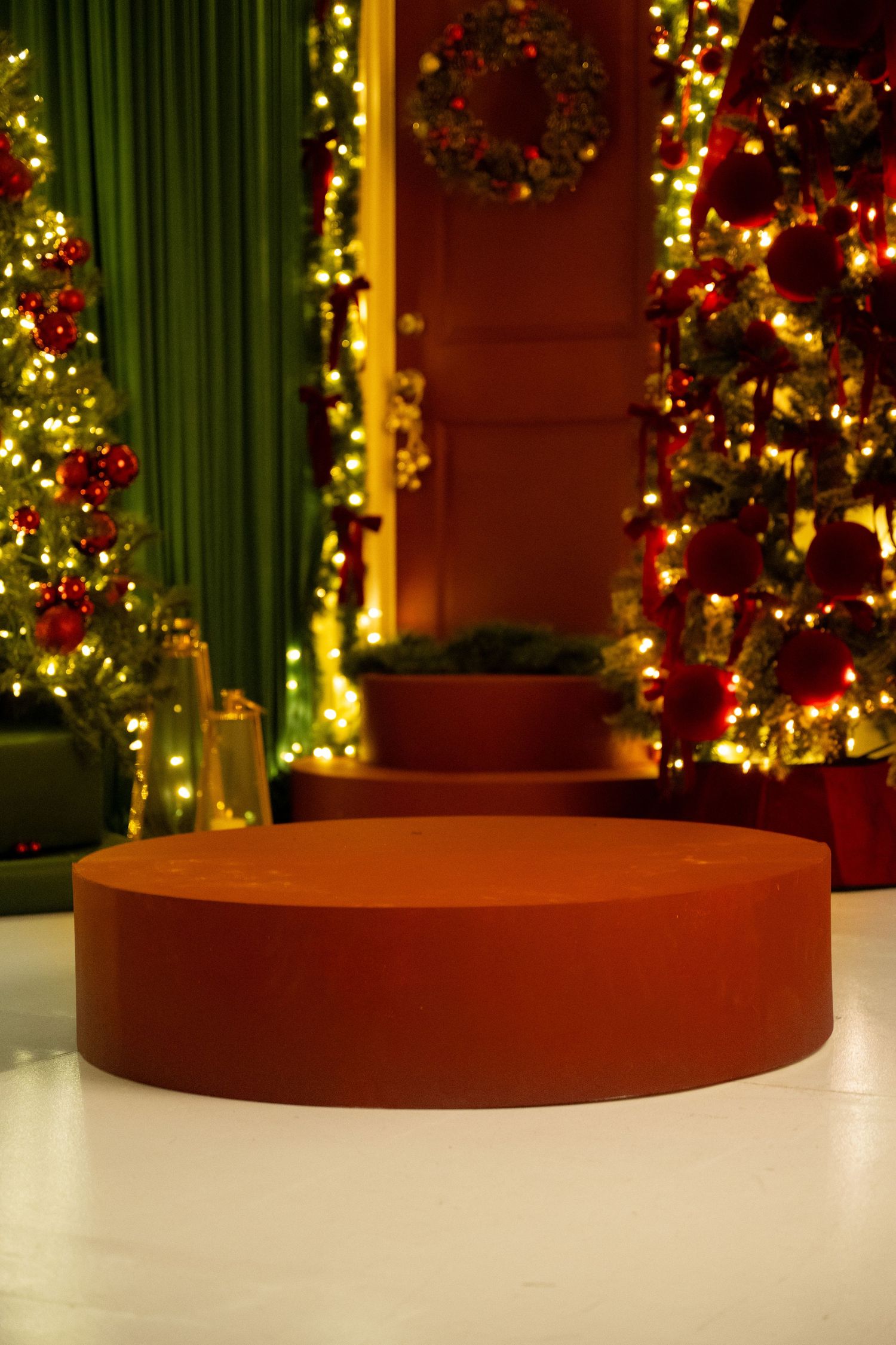 Illuminated Christmas trees with warm glowing lights create a festive holiday display against green curtains.