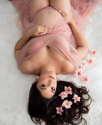 A boudoir portrait in pink tulle with dark hair splayed on white fabric and scattered cherry blossoms.