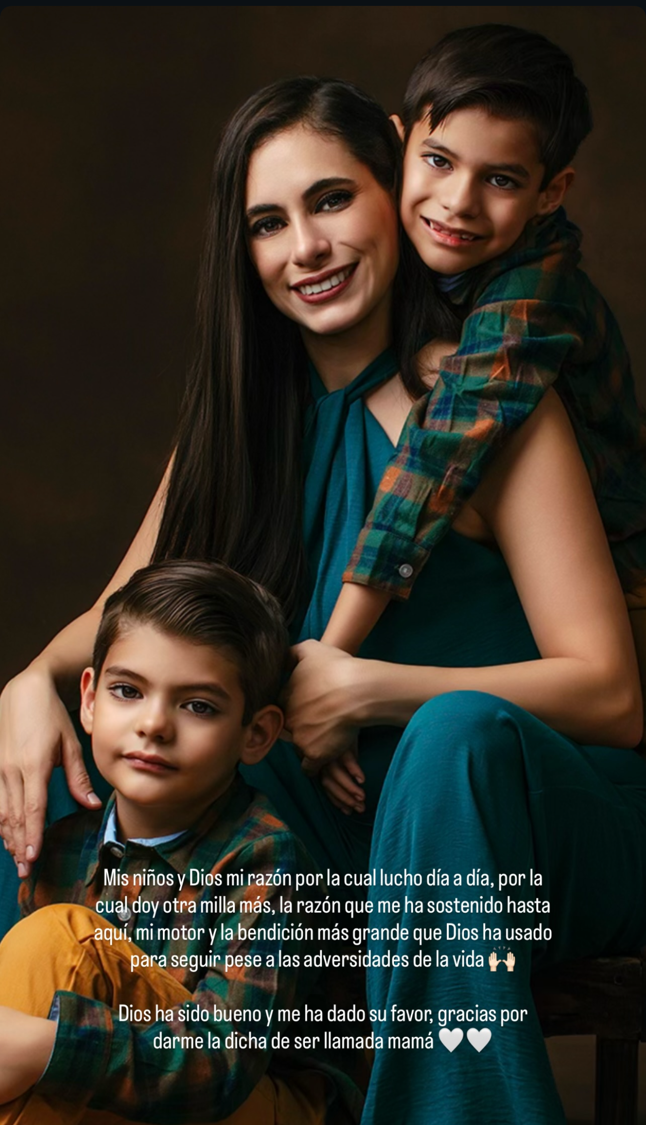 A smiling woman in teal dress poses warmly with two young boys in a professional studio portrait setting.