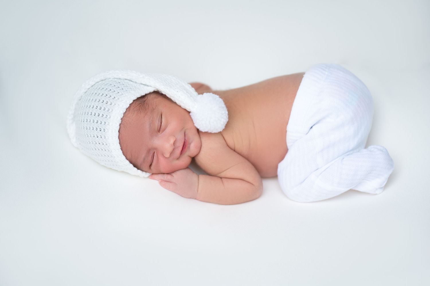 Sleeping newborn in white knit outfit against light background.