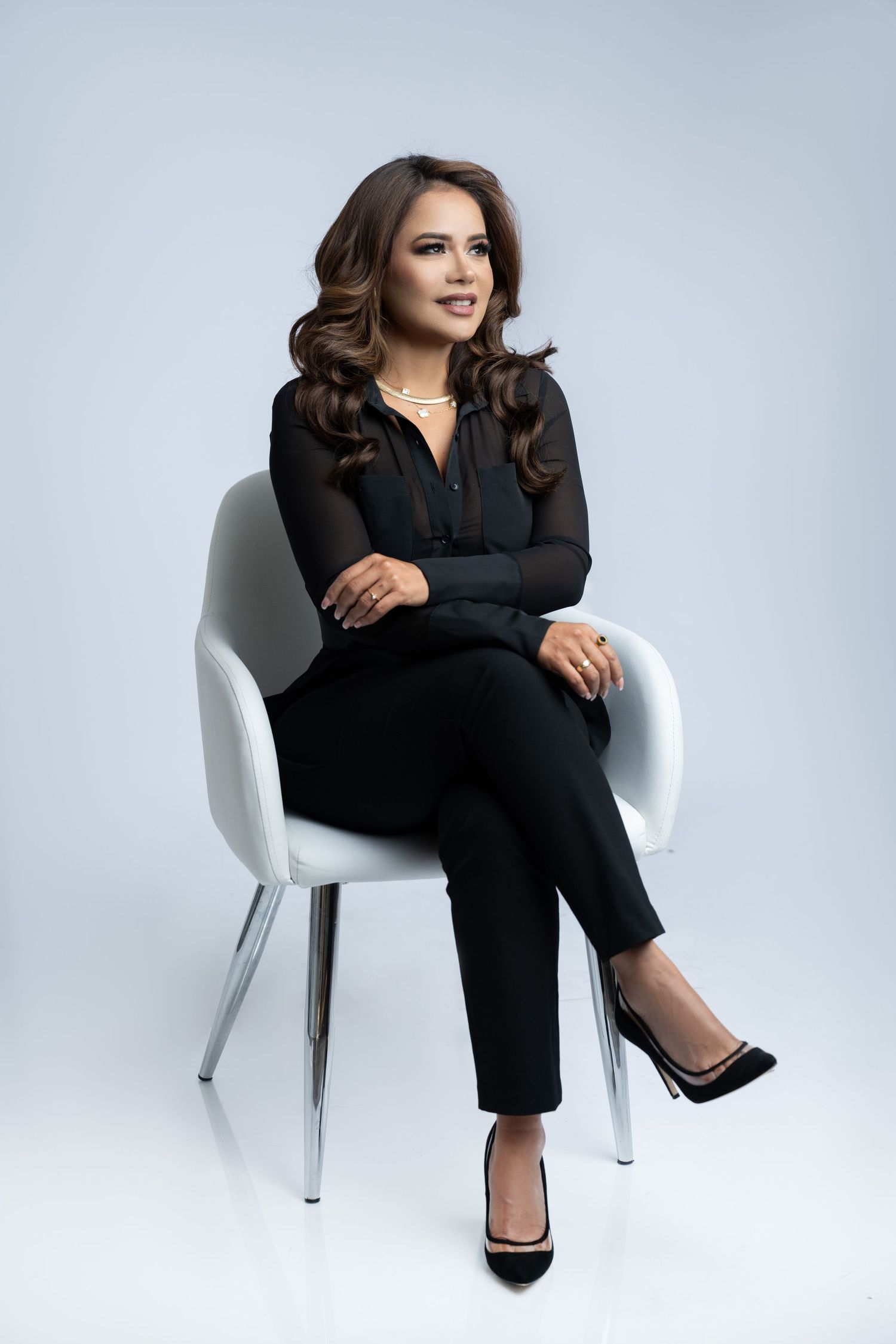 Professional portrait showing person seated in modern white chair wearing black business attire.