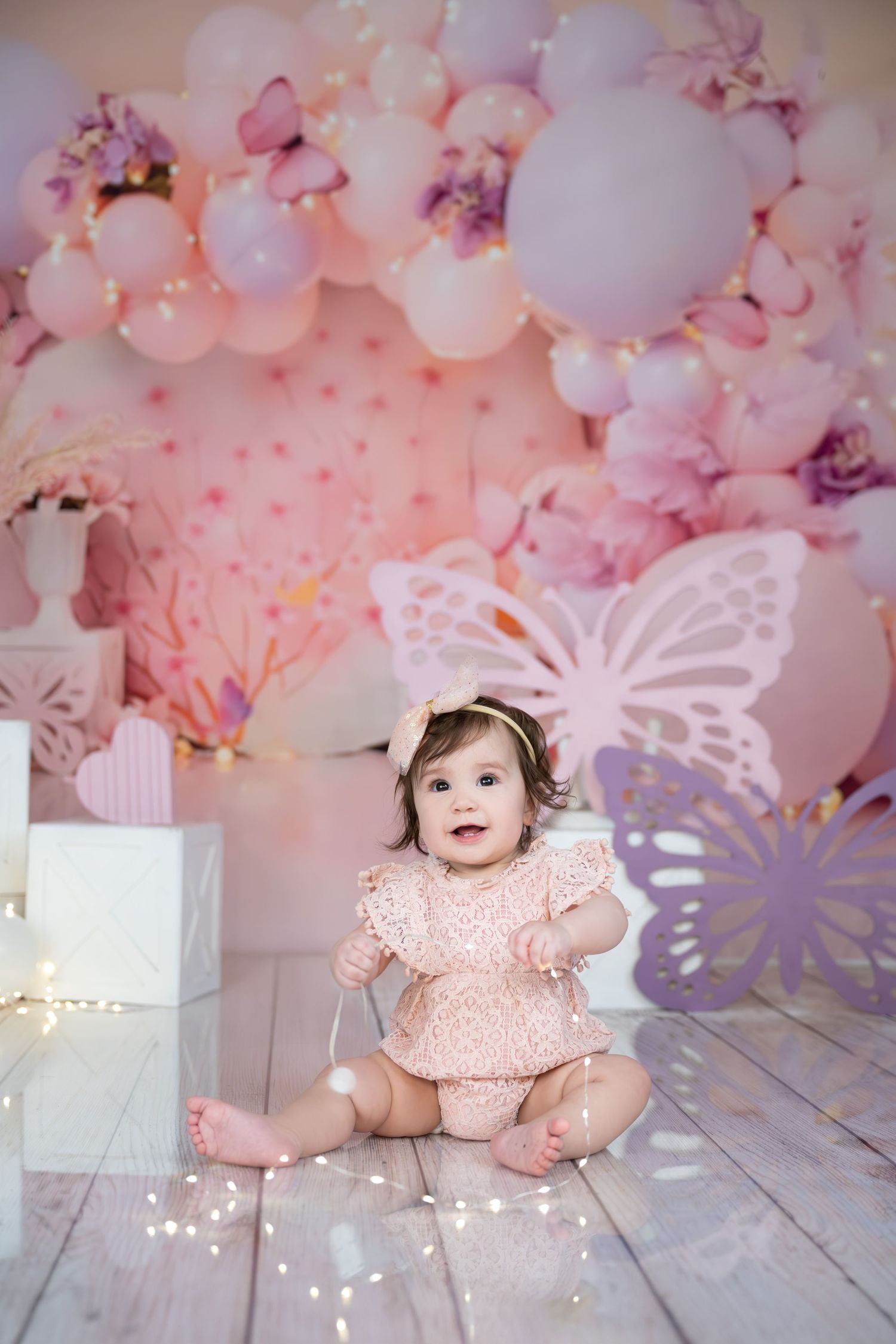 Dreamy pink balloon and butterfly backdrop with fairy lights on rustic wooden floor.