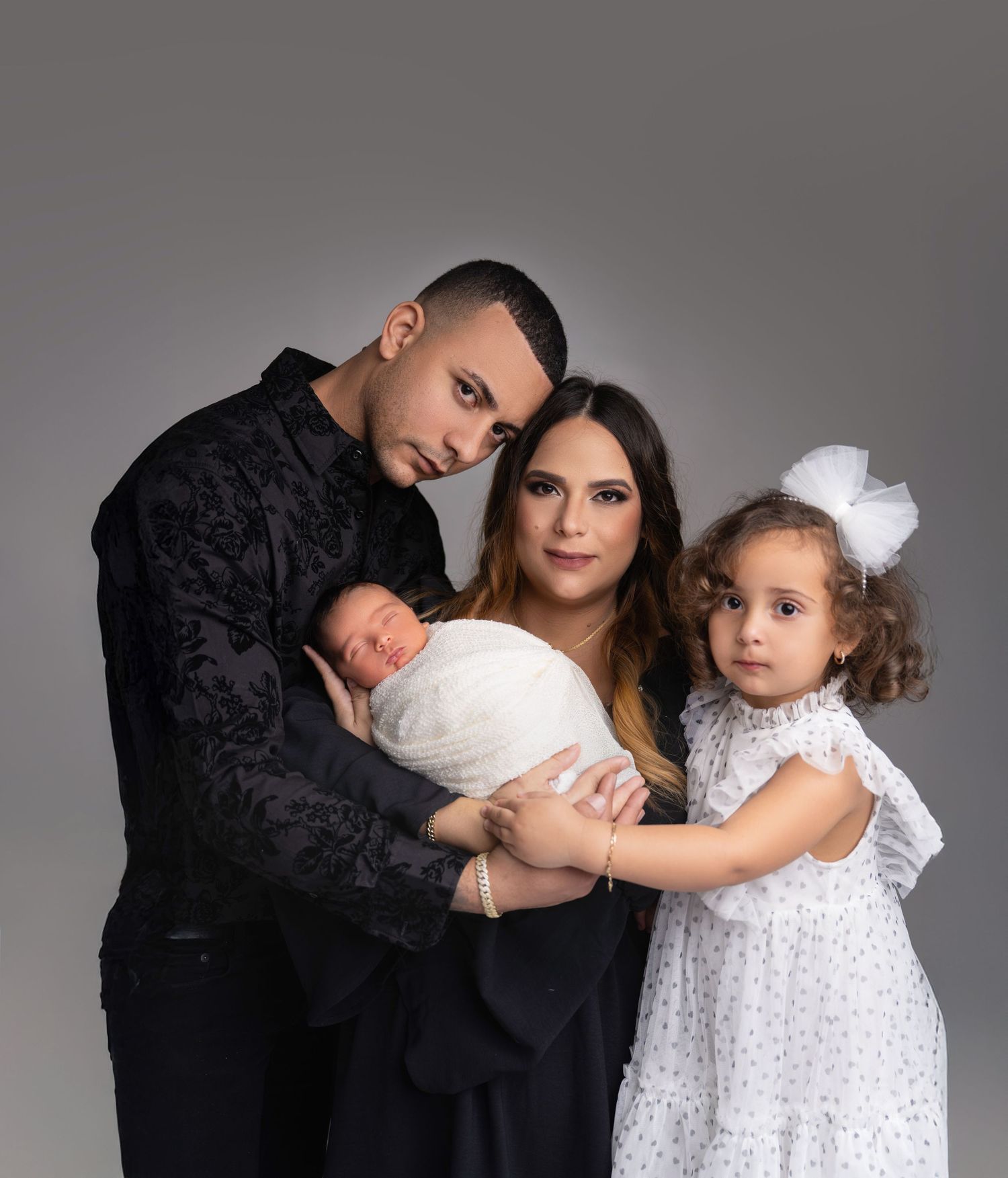 Elegant family portrait in black formal attire against grey background.