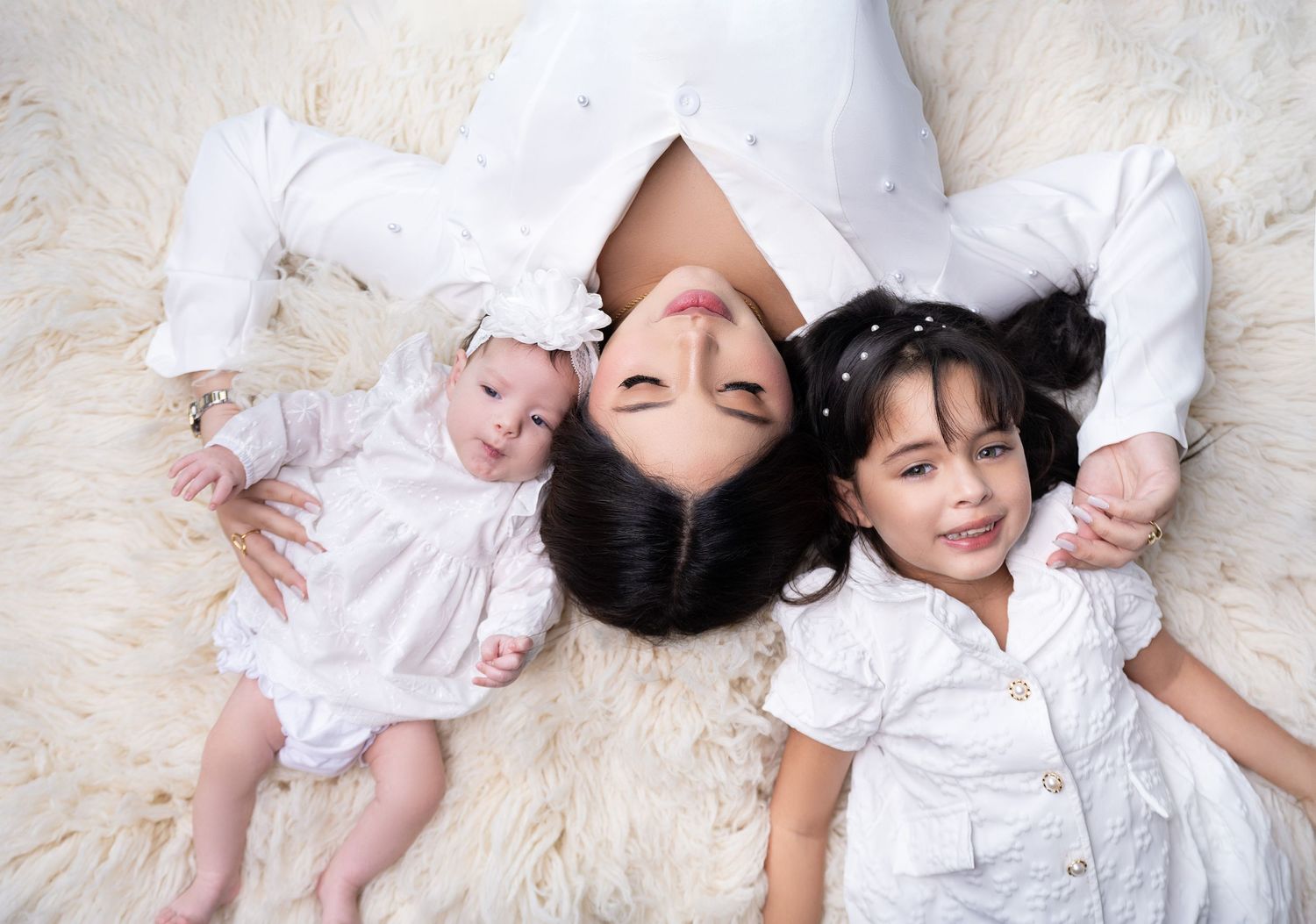 Overhead view of family in white clothing lying on cream carpet.