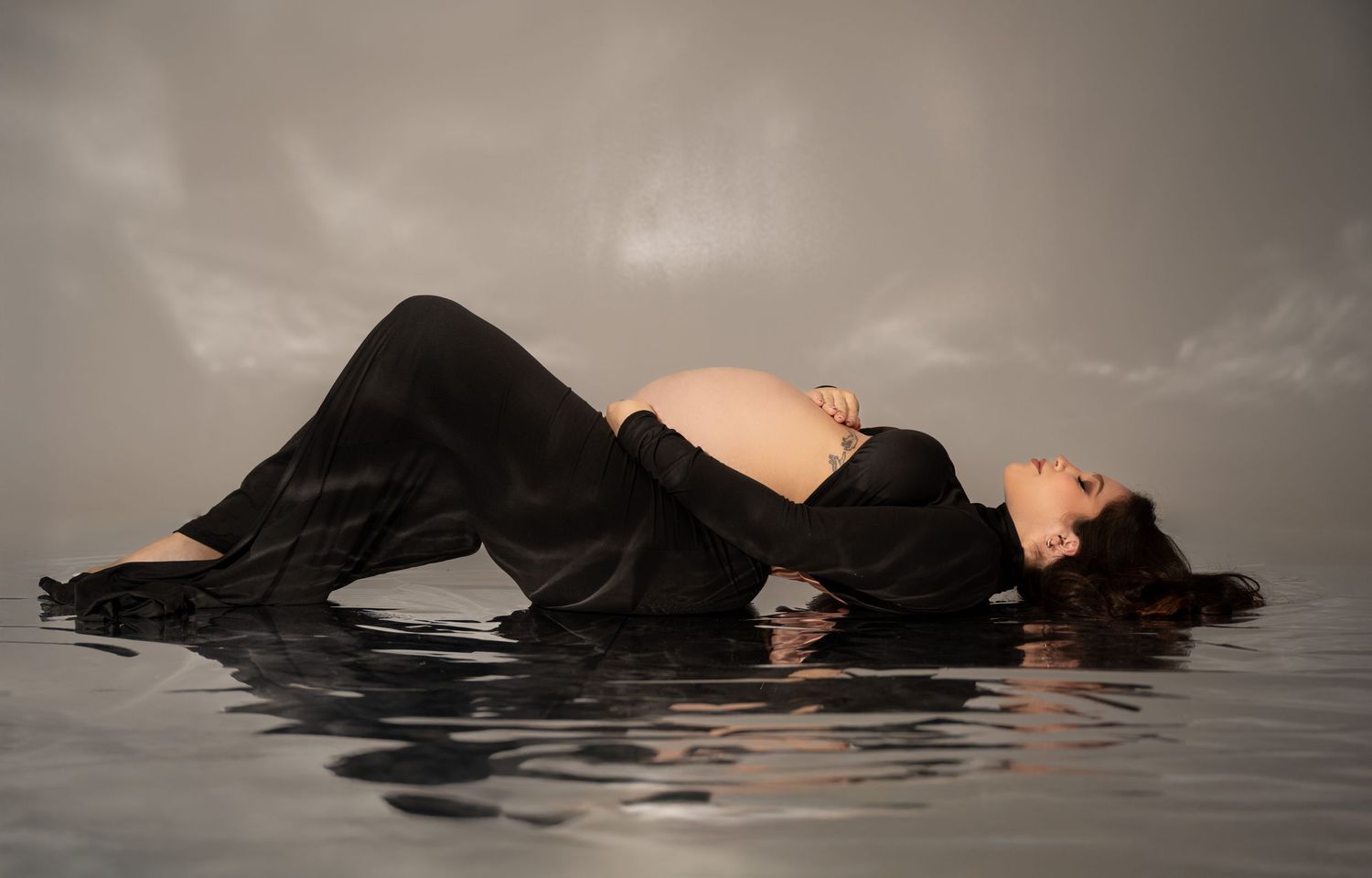 Artistic water maternity photo with reflection in black dress.