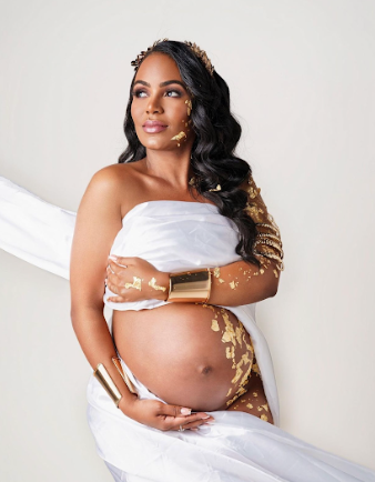 Artistic maternity photoshoot featuring white fabric draping and gold leaf accents in a minimalist studio setting.