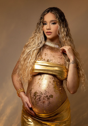 Artistic maternity photoshoot featuring gold fabric and glitter against a warm brown backdrop.