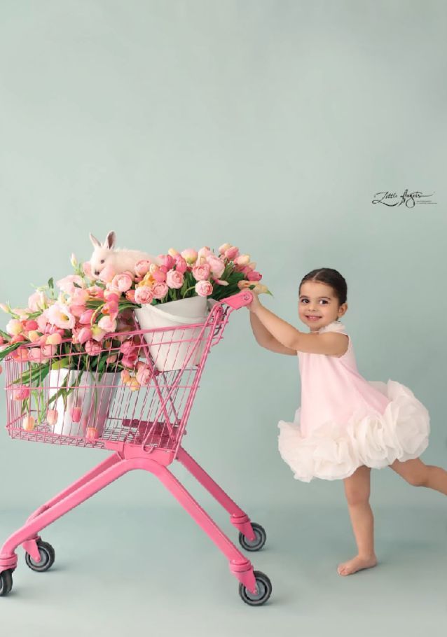 A pink shopping cart filled with fresh flowers being pushed across a mint green backdrop.