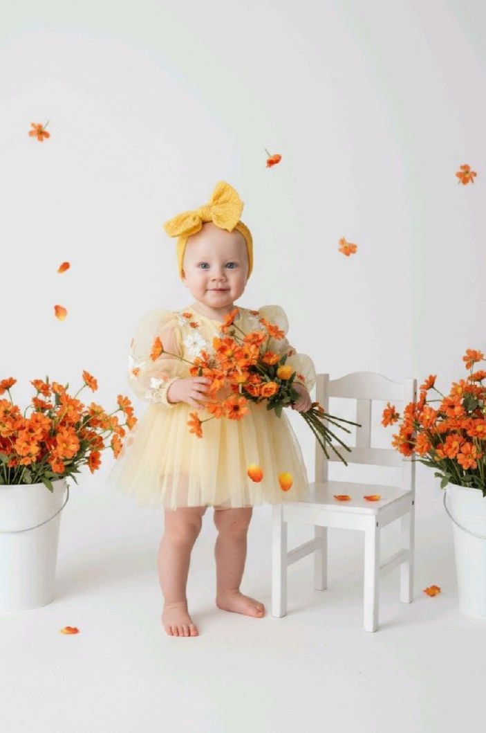 A series of photos showing a small child in a cream dress posing with orange flowers and white furniture.