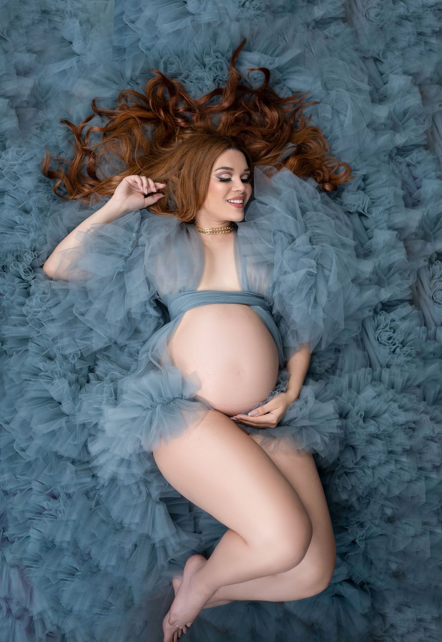 A serene maternity photo with flowing hair and blue tulle fabric creating an ethereal effect.