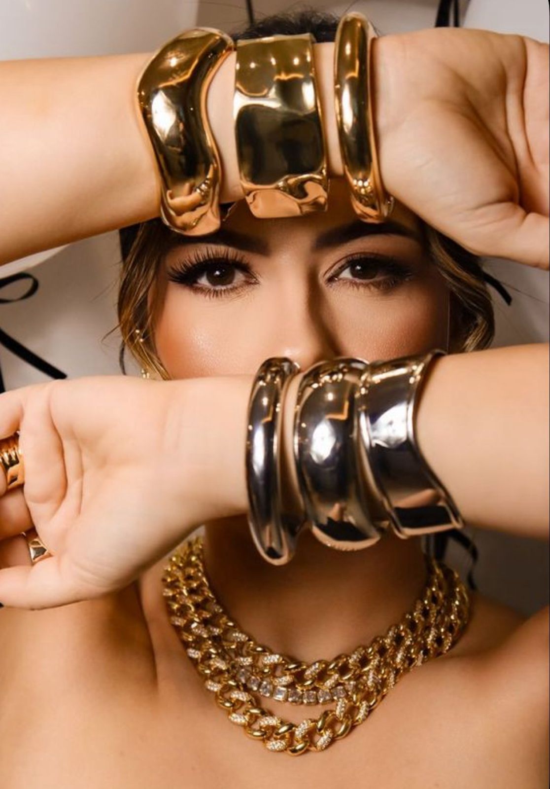 Woman posing with bold gold chunky bracelets, chain necklace, and ring, showcasing statement jewelry in a glamorous style.