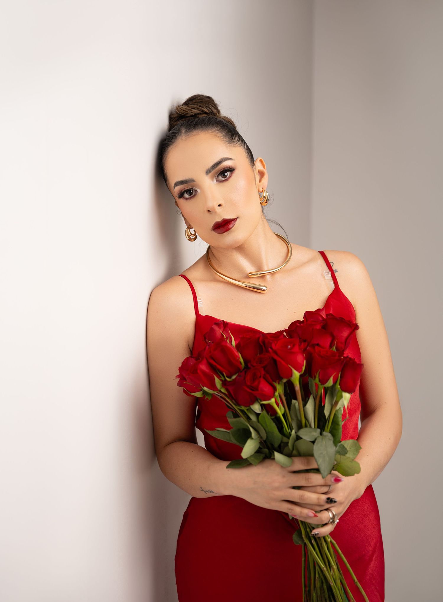 Model in red dress holds bouquet of fresh red roses against neutral background.