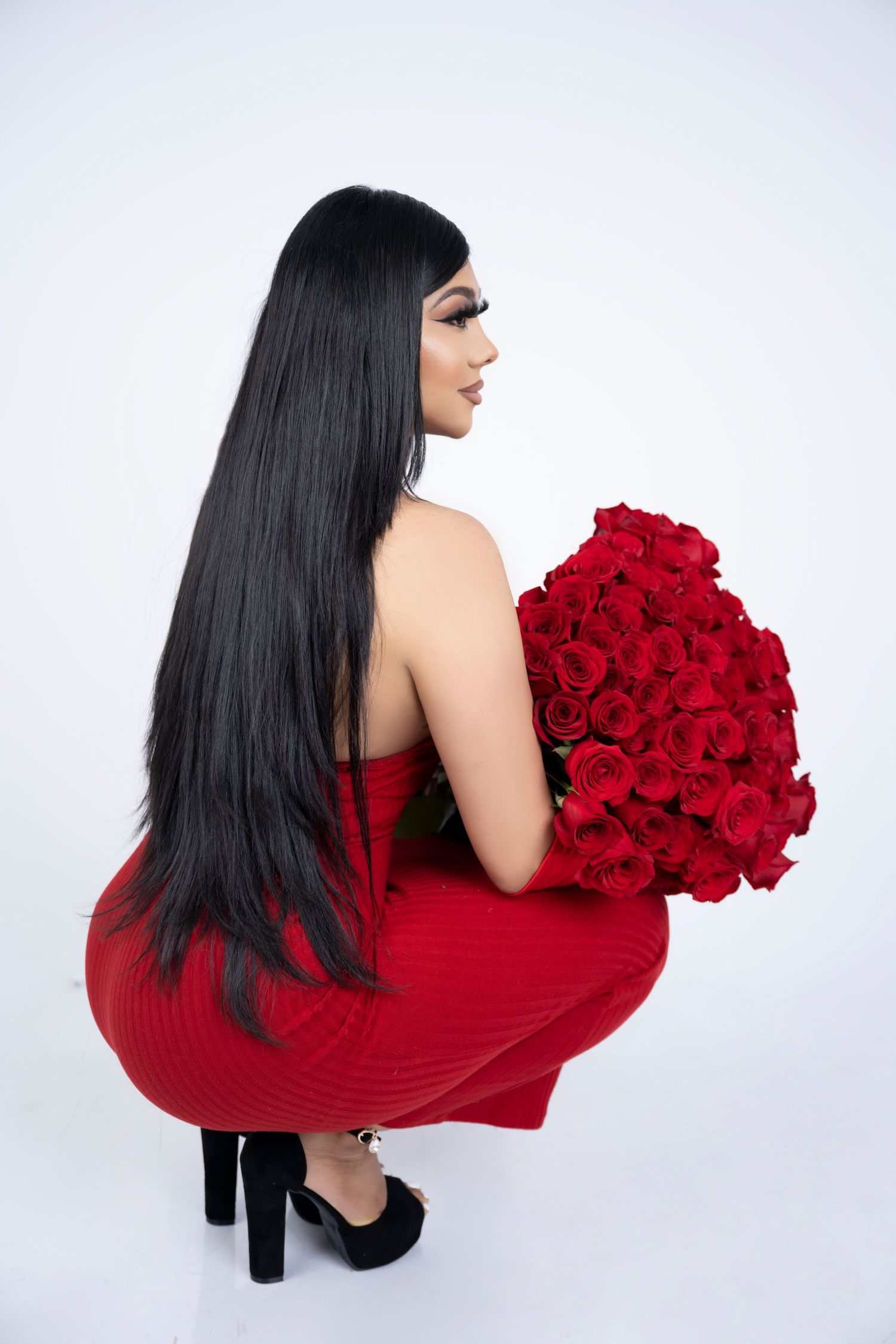 Side view of figure in red dress holding rose bouquet against white backdrop.