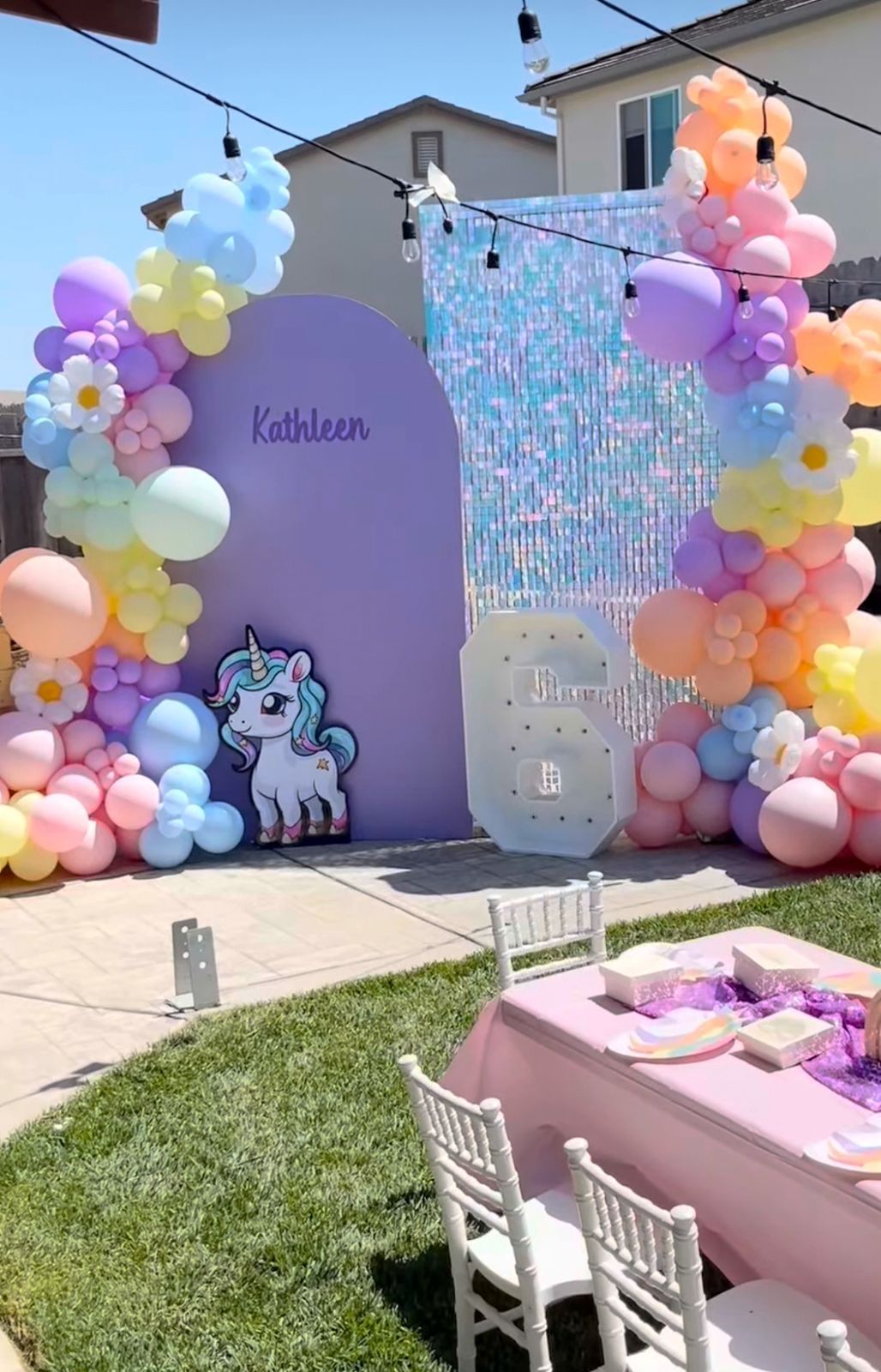 Colorful balloon arch installation with pastel pink, purple, yellow and orange balloons decorating an outdoor wall for a party setup.