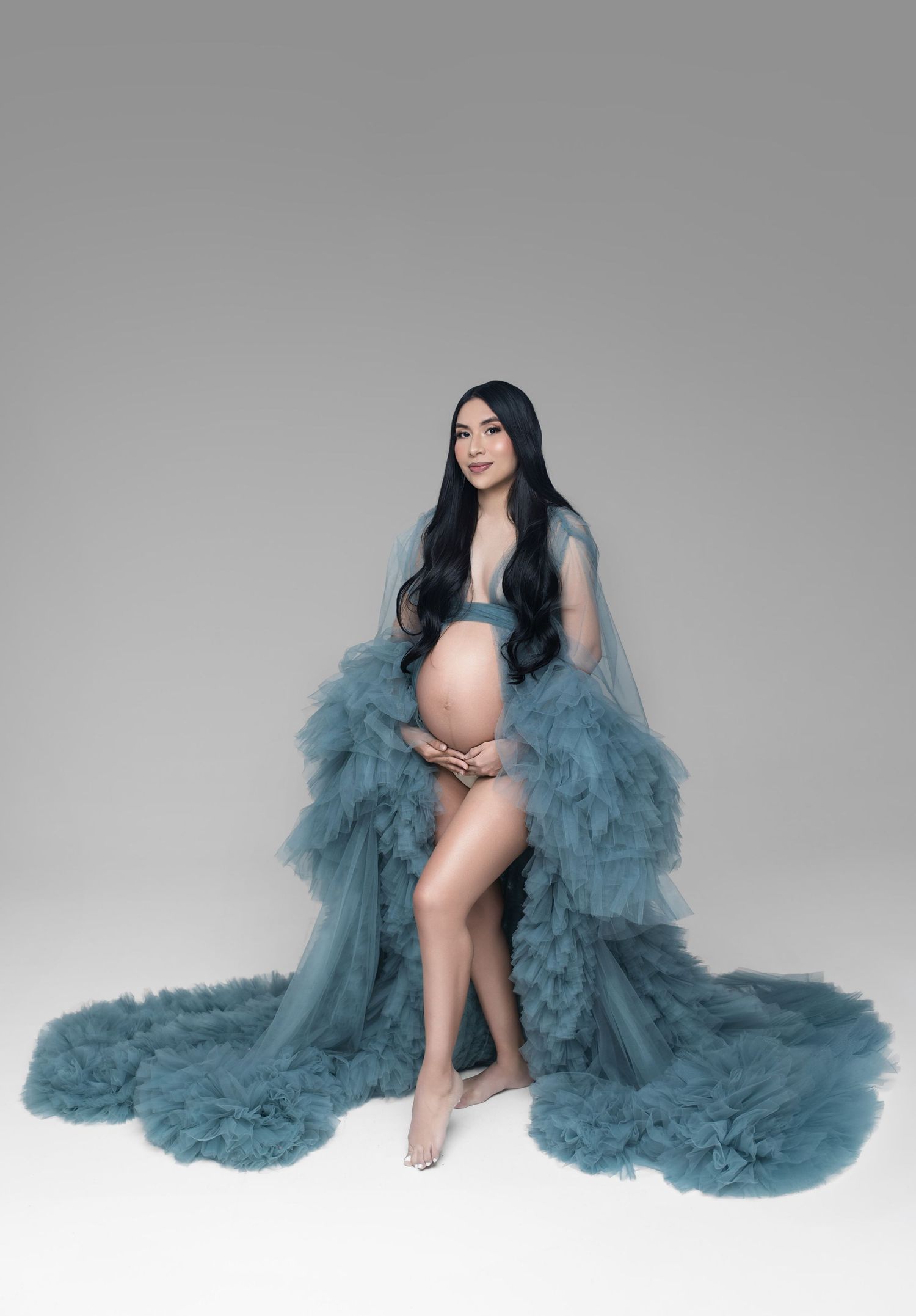 Pregnant woman in teal tulle robe posing elegantly in a studio maternity photoshoot.