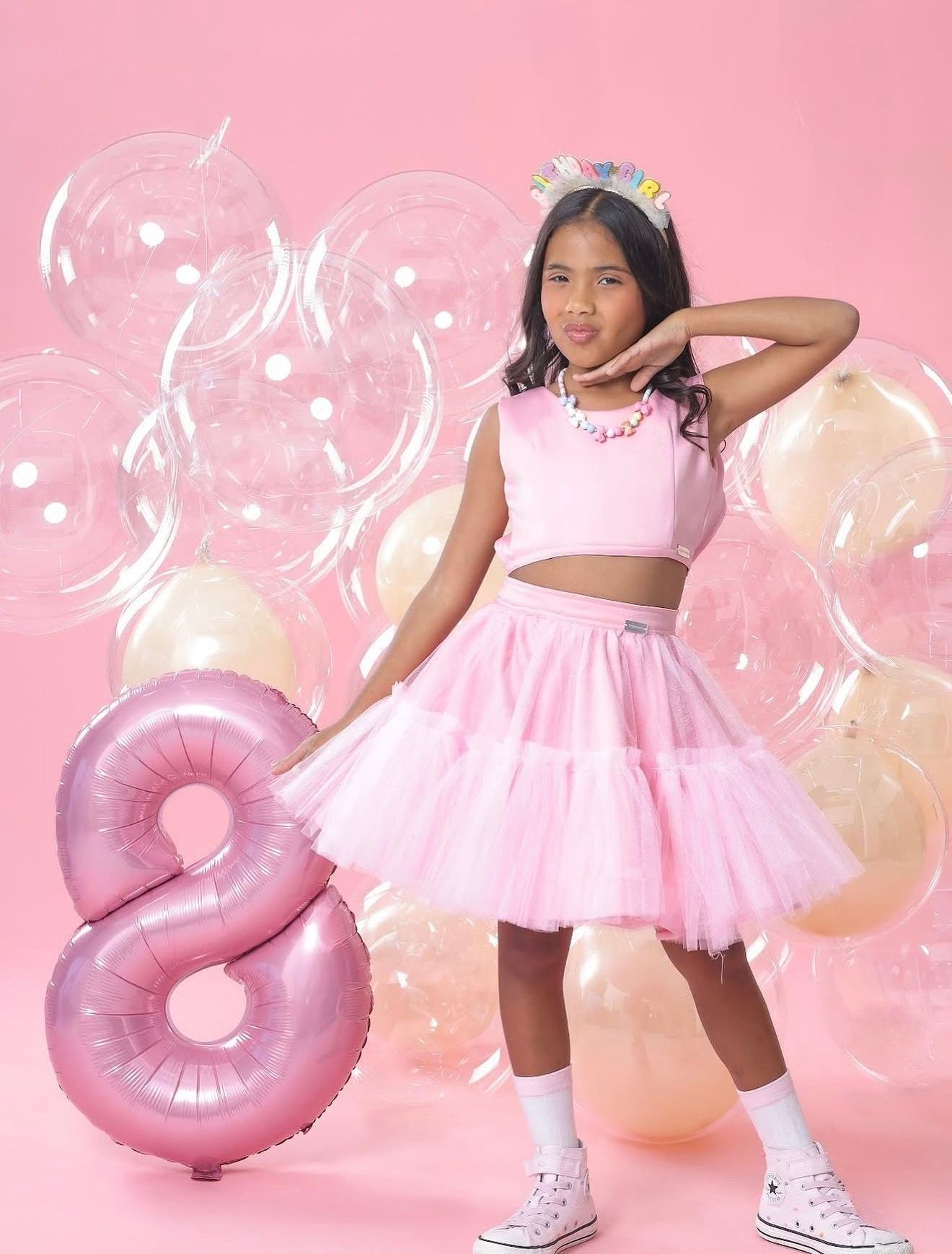 Girl in pink tutu skirt and crop top poses with number 8 balloon and colorful bubbles for birthday celebration.