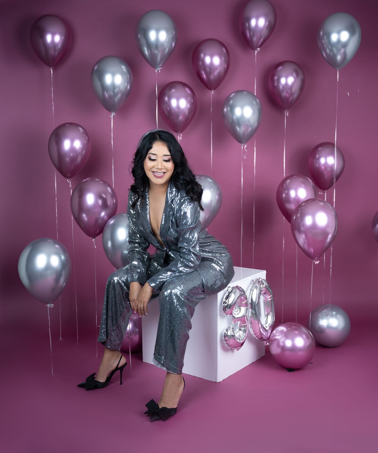Glamorous portrait with metallic balloons and silver outfit against pink background.
