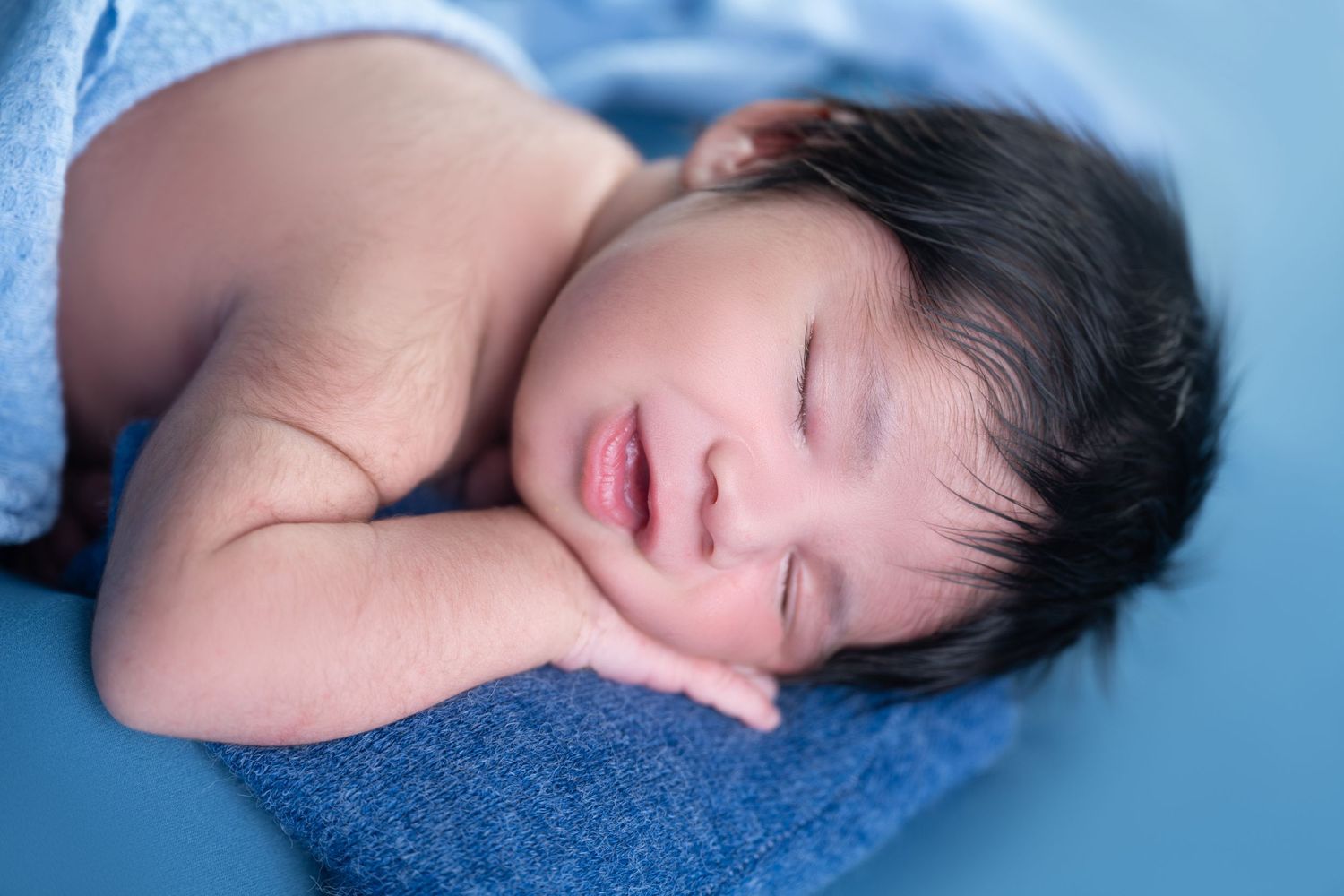 Peaceful sleeping newborn portrait on soft blue textured blanket.