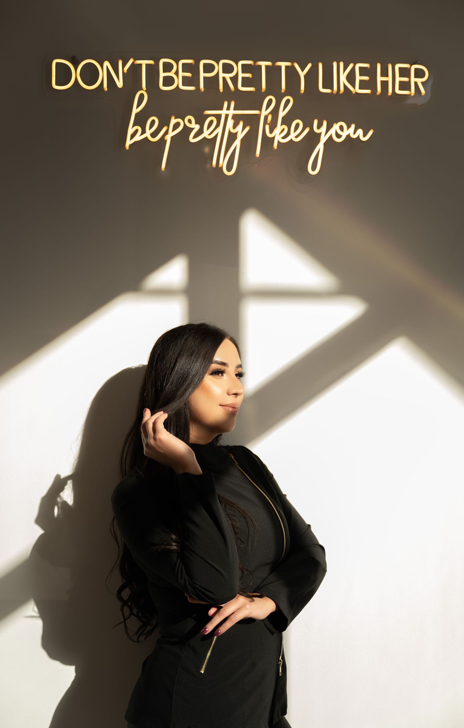 Stylish figure in black outfit poses under illuminated motivational neon sign.