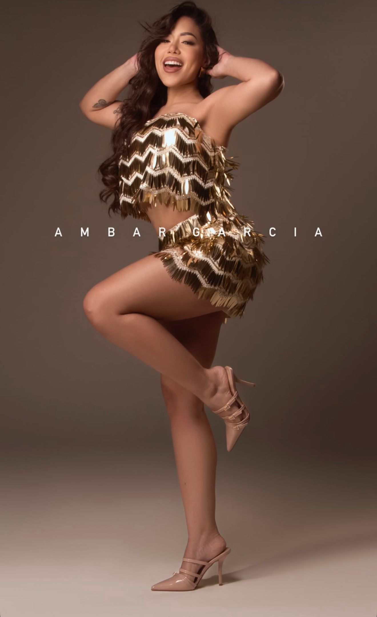 Woman in gold fringe mini dress posing confidently in heels for Ambar Garcia fashion photography.