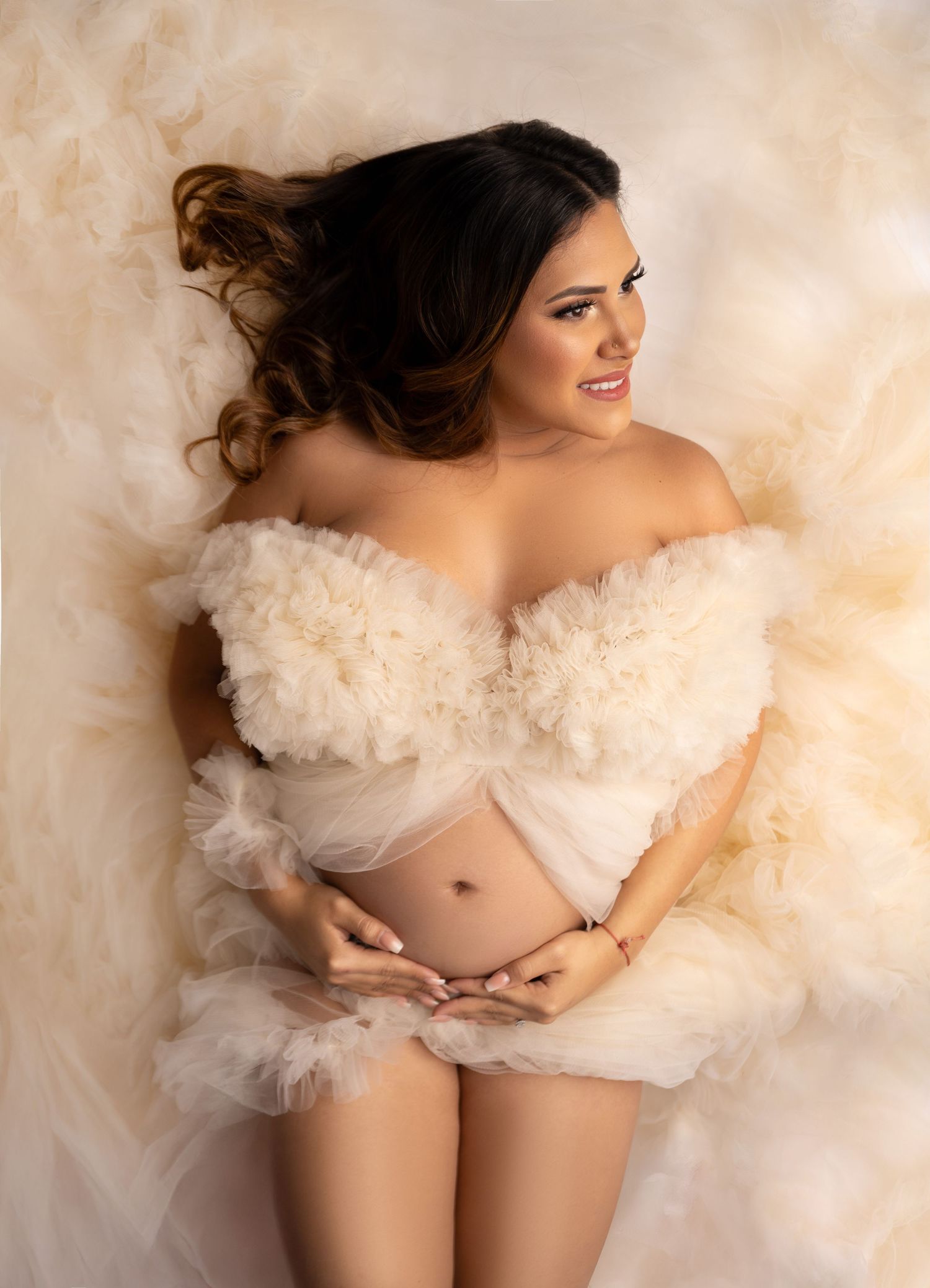 Maternity portrait with flowing white tulle fabric and soft beige background creating an ethereal romantic mood.