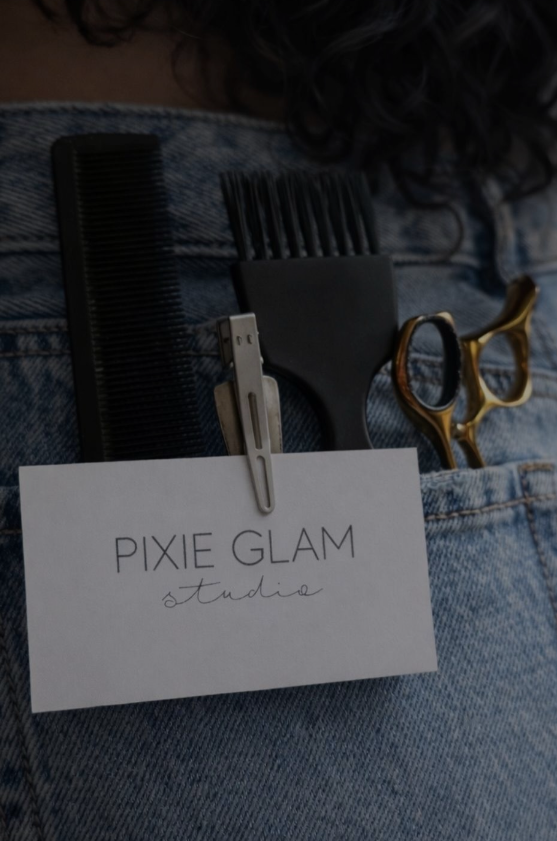 Pixie Glam Studio business card tucked in denim pocket with gold scissors and hair combs.