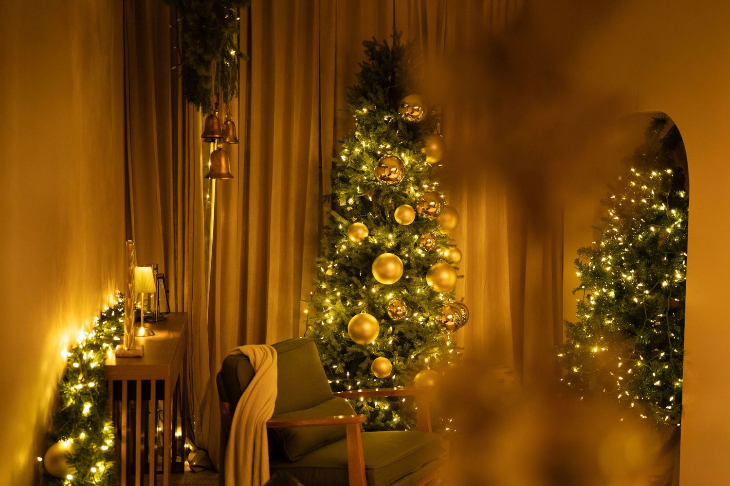 A warmly lit Christmas tree decorated with gold ornaments and lights glows in a cozy corner of a room.