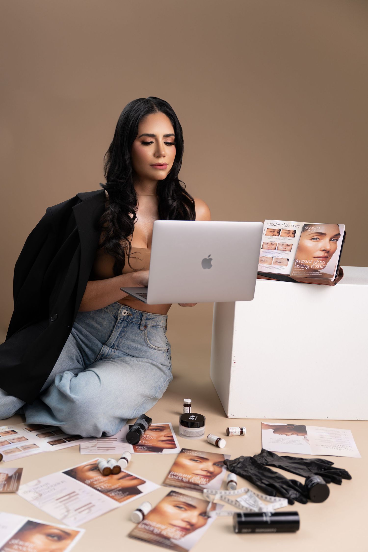 A person in black clothing lies on the floor with a MacBook laptop and scattered photographs around them.