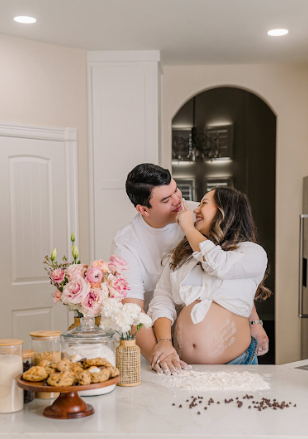 Romantic engagement photoshoot in a kitchen with baked treats and pink floral decorations on the counter.