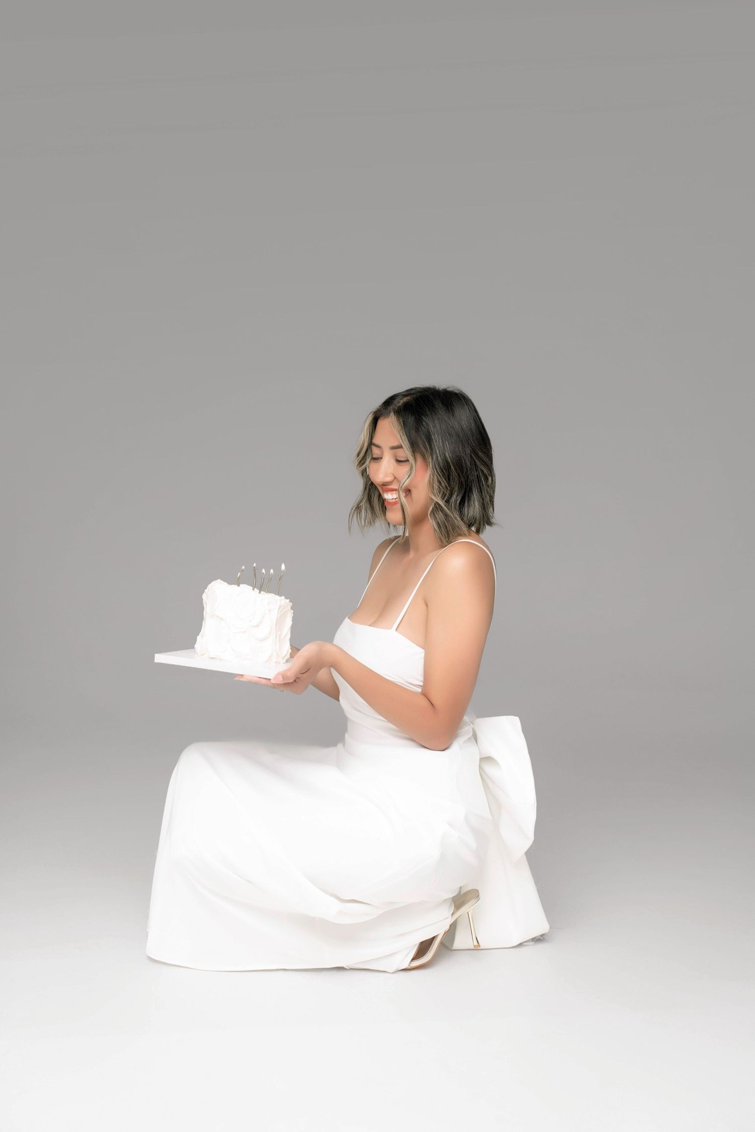 A series of photos showing a person in white dress sitting on floor against grey background, expressing joyful emotions.