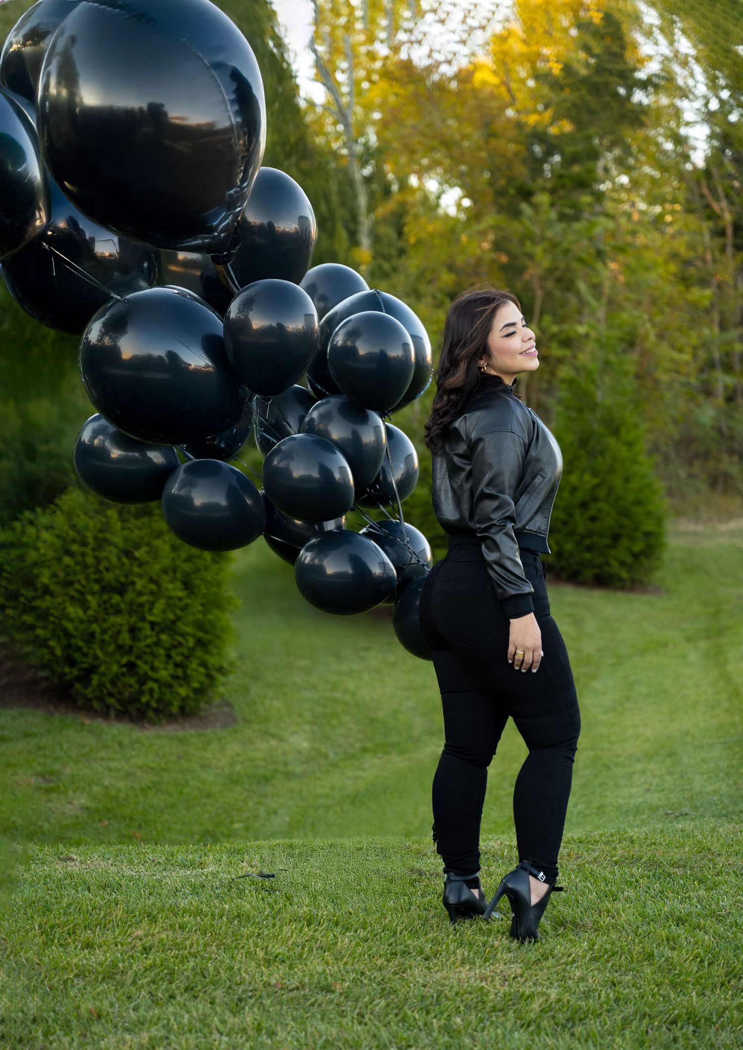 Black balloon arrangement and matching outfit in outdoor garden setting.