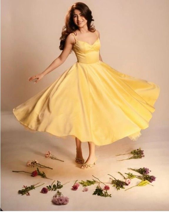 Woman twirling in a yellow midi dress surrounded by scattered flowers on a light background.