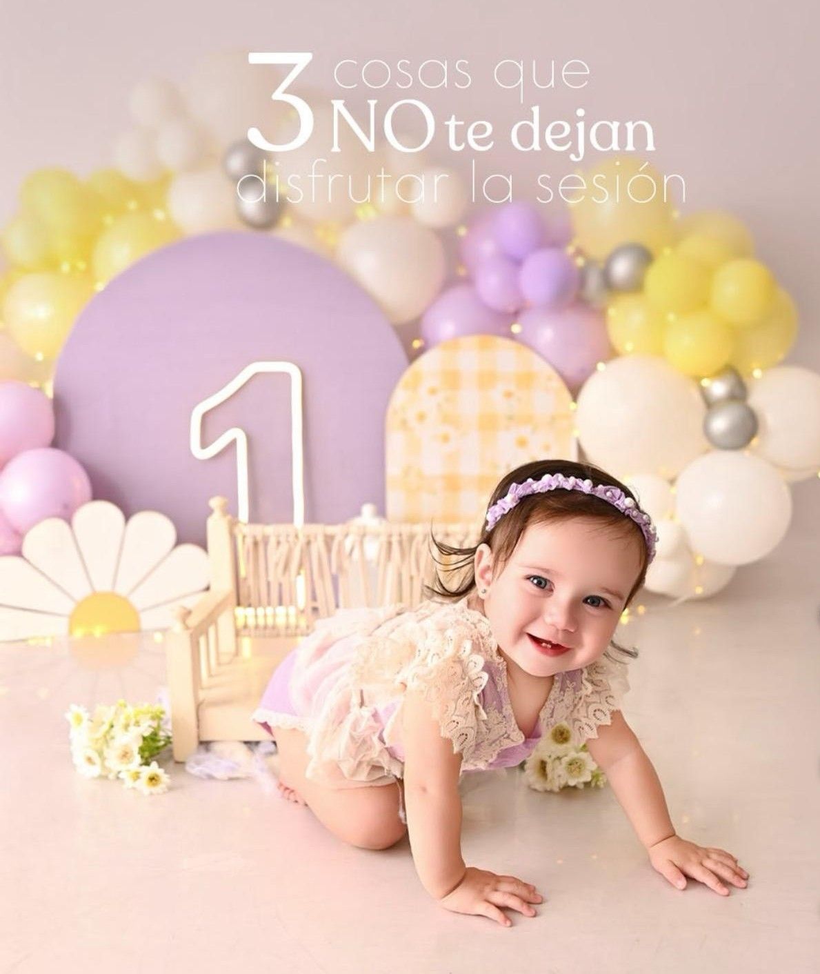 A smiling baby girl crawls on the floor at a first birthday cake smash session with purple and yellow balloon decorations.