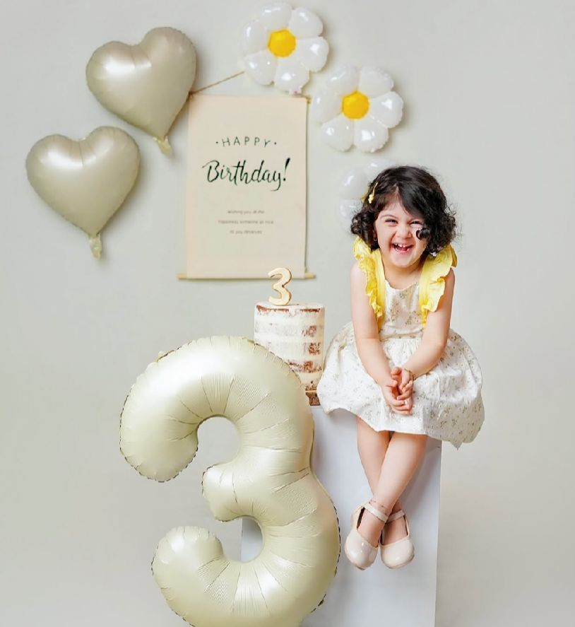 Birthday celebration setup with white daisy decorations and silver heart-shaped balloons against a light background.