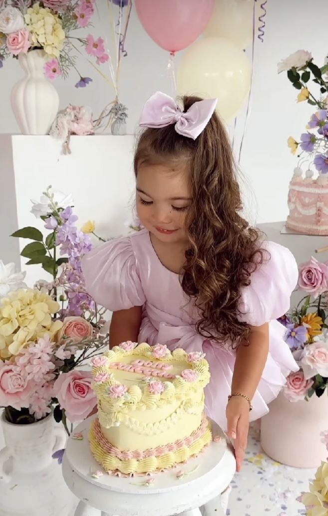 A series of photos showing a child in a pink dress looking at a decorated yellow birthday cake with flowers.