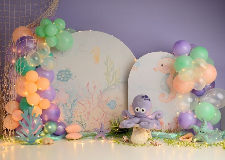 Under-the-sea themed birthday cake smash backdrop with pastel balloons, octopus plush, seahorses, and twinkling fairy lights.