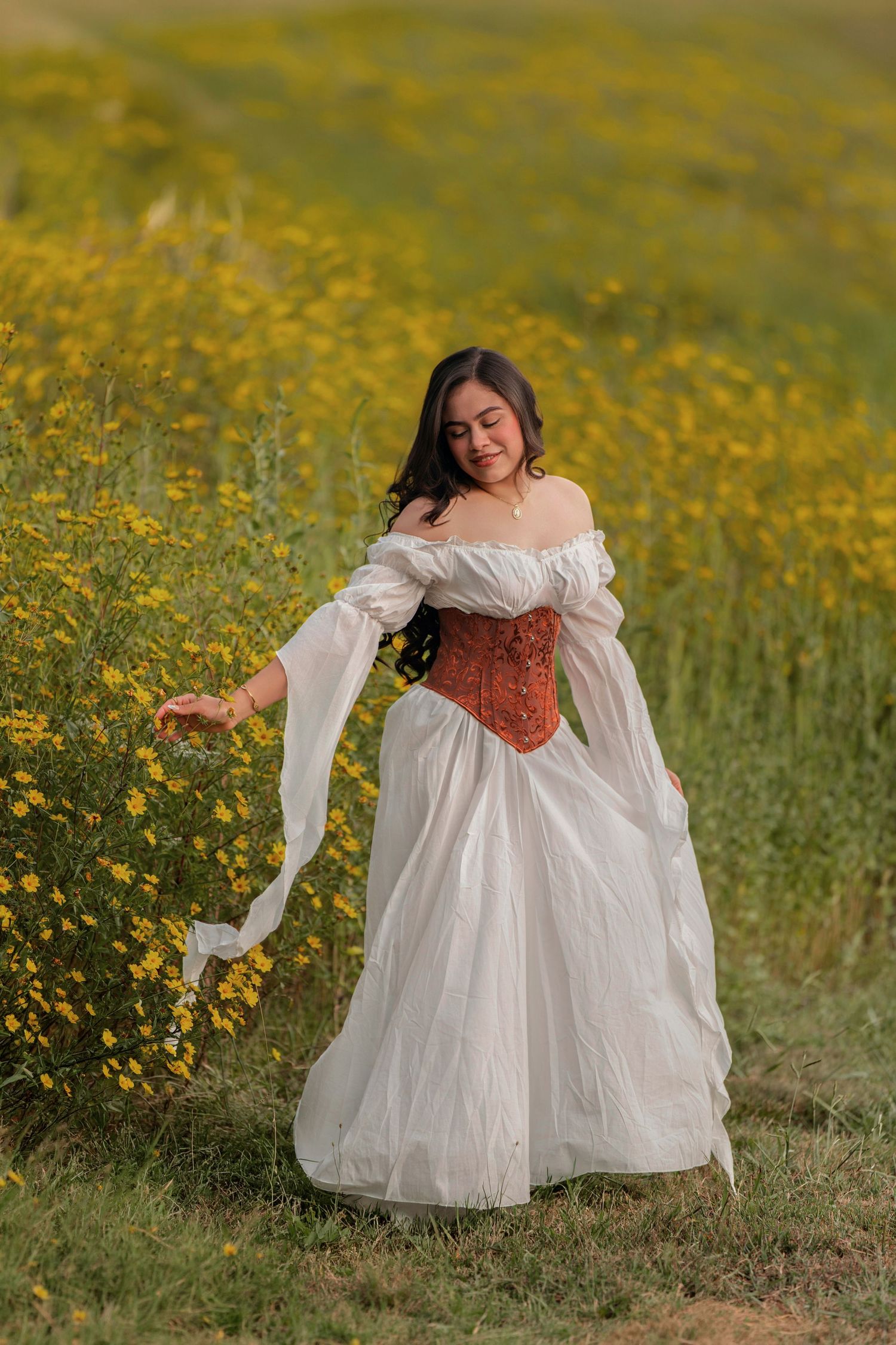 Woman in white Renaissance gown and red corset smiling in a field of yellow wildflowers.