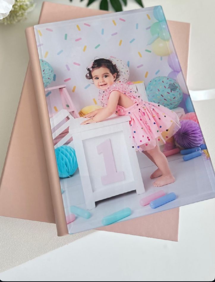 A series of pink and pastel-colored birthday cake smash photo session prints displayed on a beige surface.