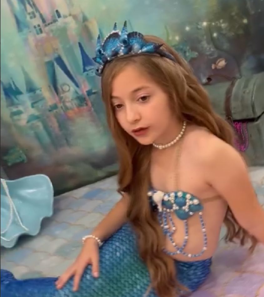 Person in a sparkly blue mermaid-style dress poses against an ethereal aqua background.